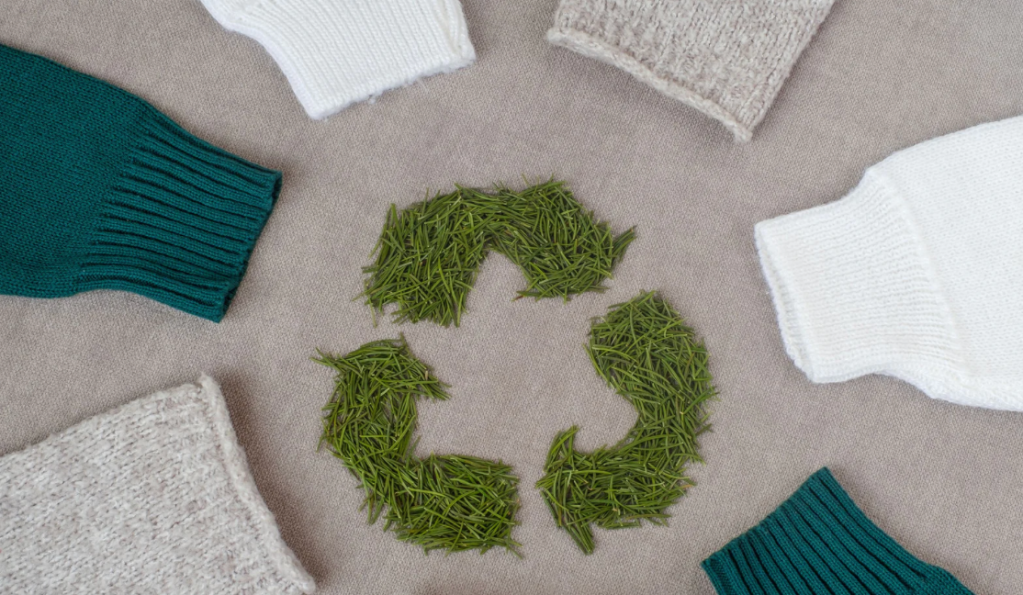 A CIRCLE OF CLOTHING PEICES AROUND THE RECYCLE SYMBOL THAT IS MADE OF A GRESSY MATERIAL
